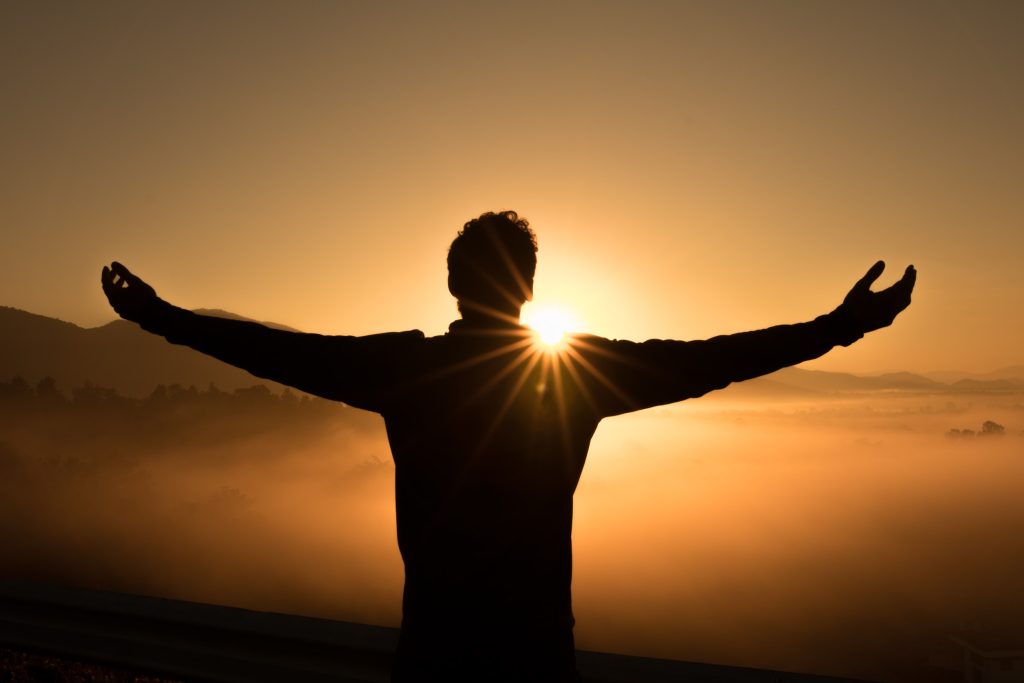 Wellness Journey - Man standing in front of the sun with open arms